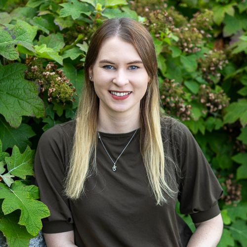 MGI doctoral student Julia Kelliher smiles at the camera. There is a plant behind her. 
