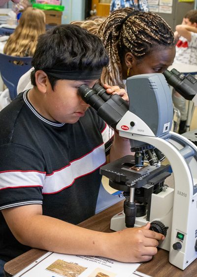 A student looks through a microscope and Djeneba Diallo looks through another microscope. 
