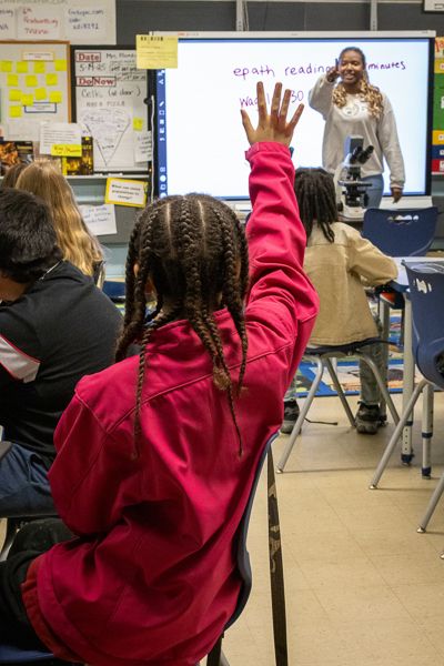 A student raises her hand and Djeneba Diallo calls on her during the outreach program. They are in an elementary classroom. 
