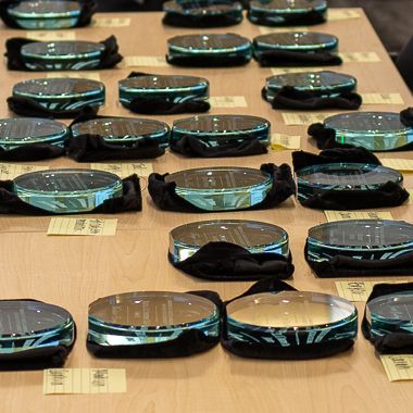 A collection of engraved glass awards sits on a table. There are post-it notes throughout with writing on them as well. 
