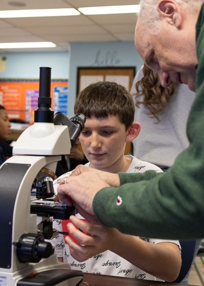 A student looks on as Dr. Hardy helps him load a slide into the microscope. 
