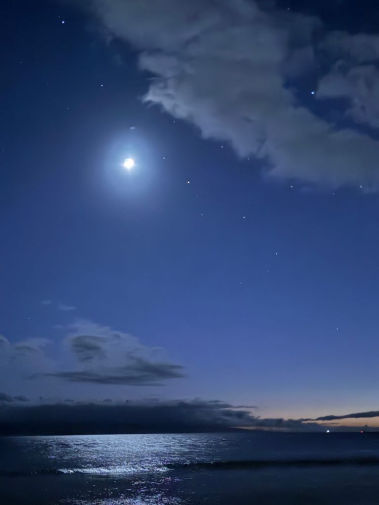 crescent moon reflects on water below the night sky