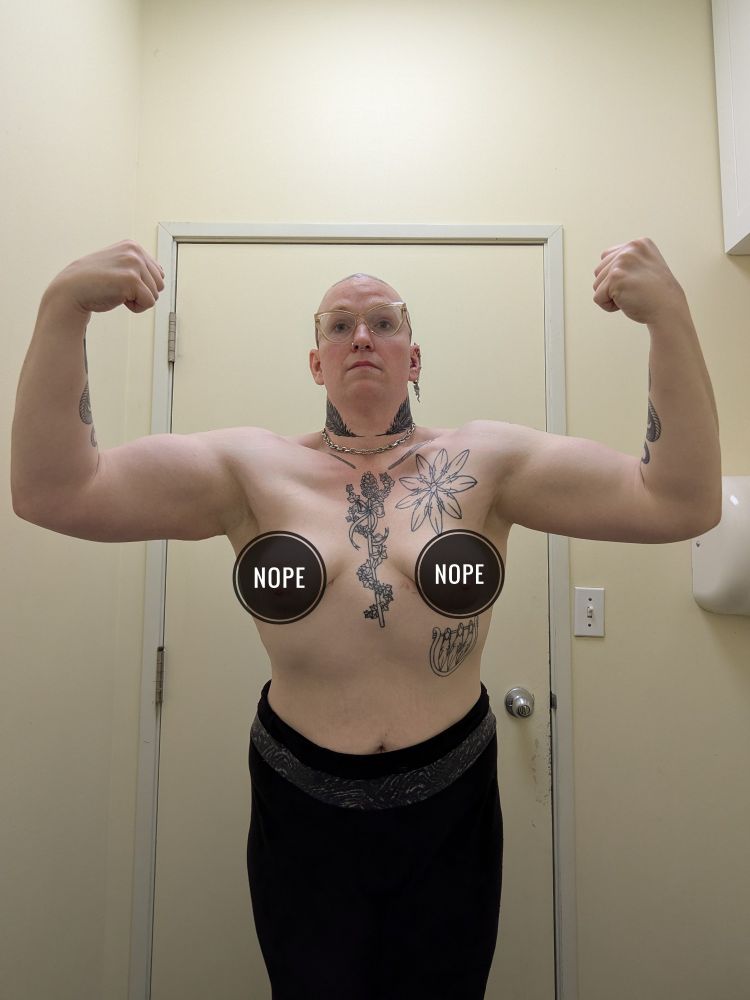 A topless bald tattooed white woman visible from the knees up flexing her arms and her chest. Black circles saying "NOPE" have been edited over her breasts.