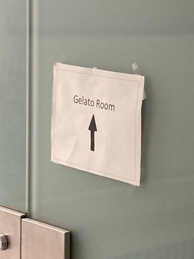 A paper sign, taped onto frosted glass, which says “Gelato Room” with an upward pointing arrow. 