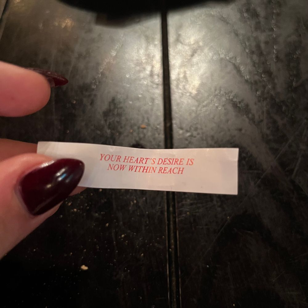 It’s a fortune cookie fortune that says “Your heart’s desire is now within reach,” held between Abi’s burgundy acrylic nails 