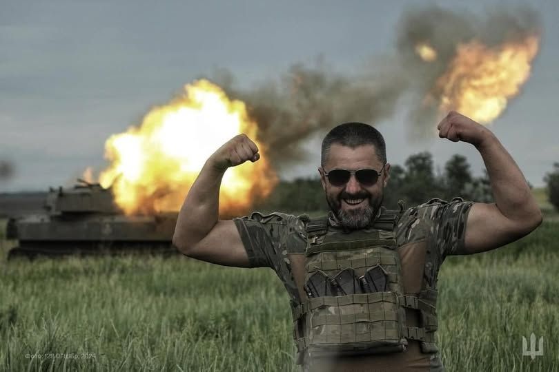 A russian tank exploding behind a Ukrainian soldier flexing his mucles