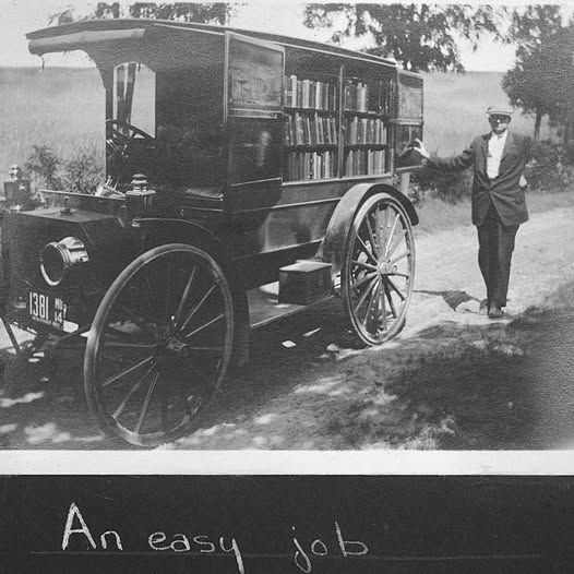 A black and white photo of an old jalopy filled with books and a man standing next to it.  At the bottom of the photo it says, "An easy job."