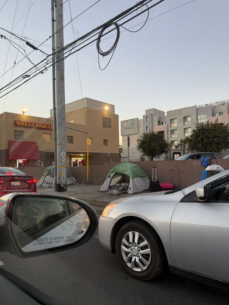 It’s just beyond my capacity to accept. Apartment homes and one of the largest banks create the background for unhoused people sleeping in tents on the sidewalk at a busy intersection. 