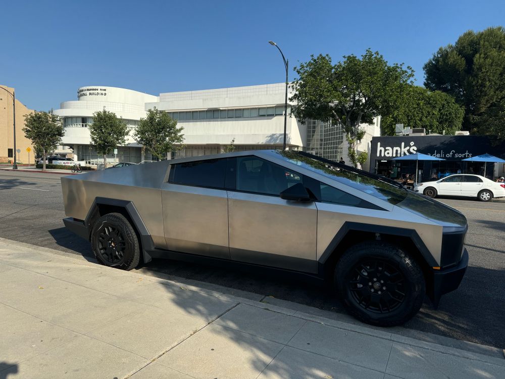 A photo of a parked Cybertruck. It is a matte silver with all black wheels.