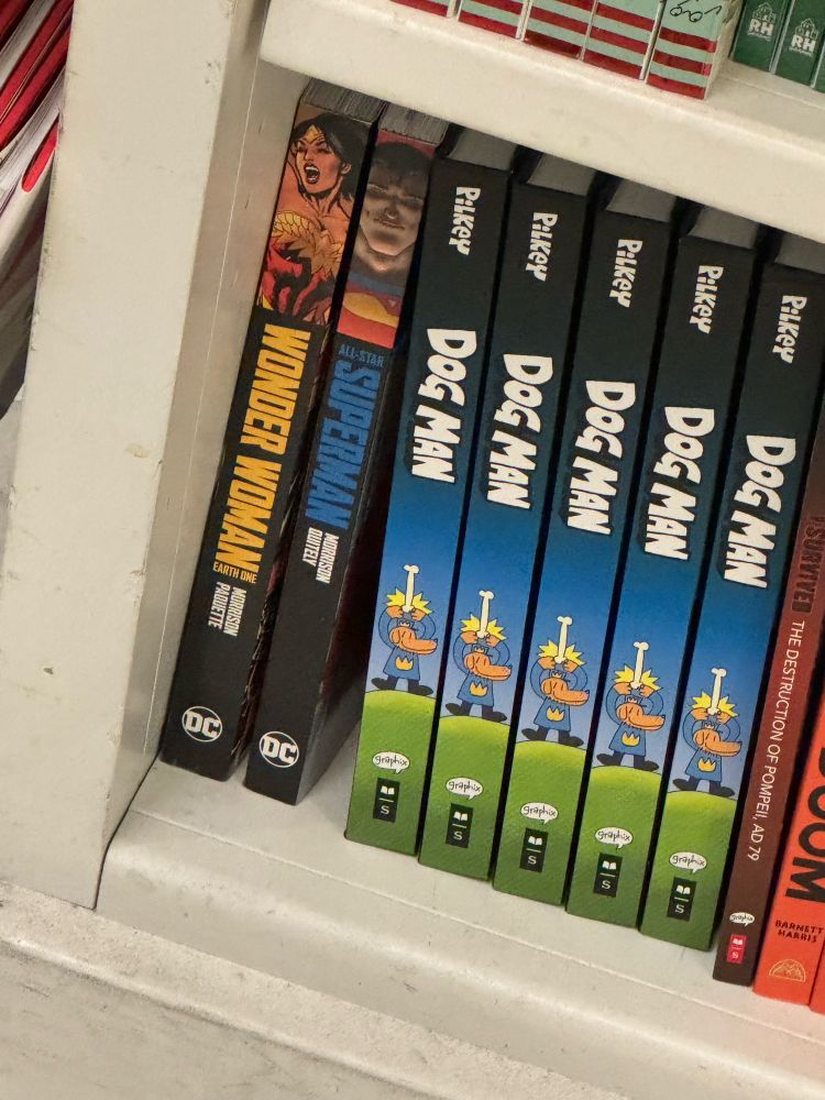 A close-up of a bookshelf in a shop at LAX. Next to several digest-sized graphic novels of Dog Man are two DC Compact Comics, which are the same size. One of them is Wonder Woman Earth One, and the other is All-Star Superman. 