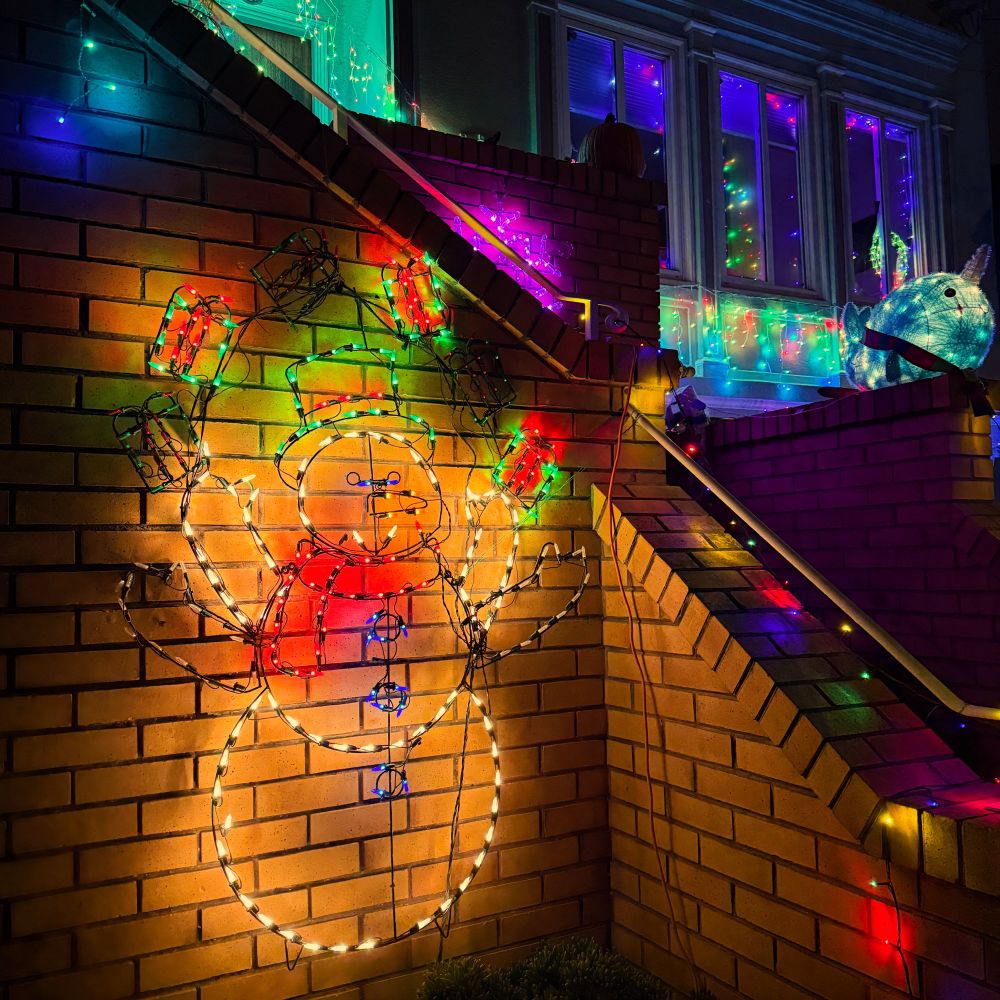 Holiday lights of a snowman juggling presents against a brick staircase