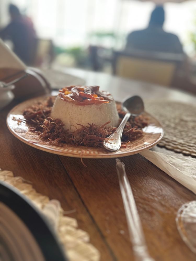 Prato de arroz de hauçá. Arroz de coco em formato de pudim, rodeado de carne seca desfiada com camarões secos por cima. 