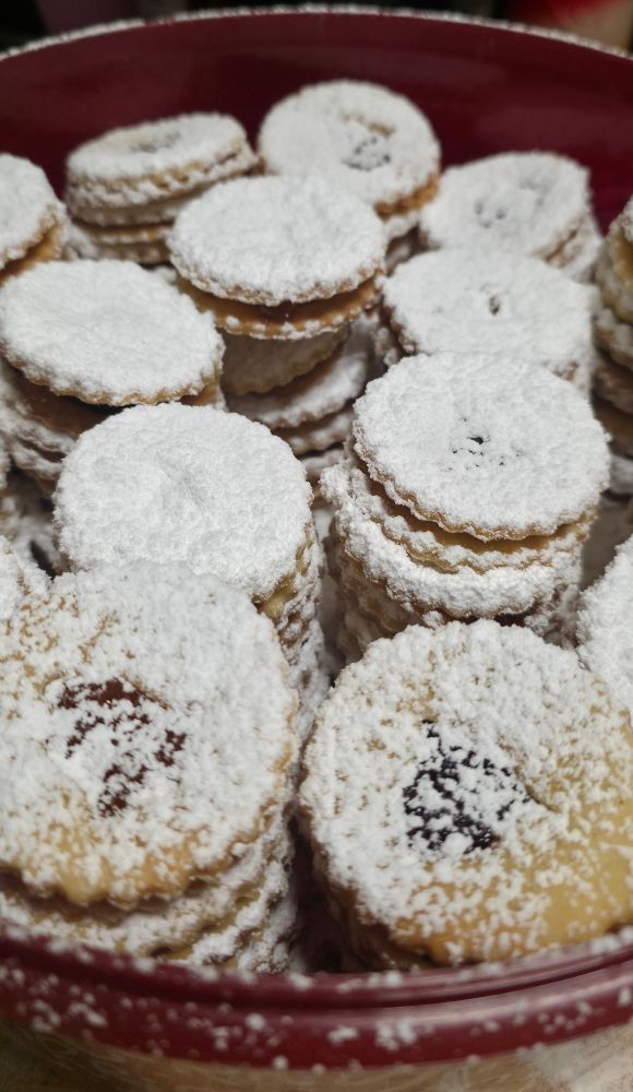 Fertige, mit Puderzucker bestreute Spitzbuben in einer roten Keksdose.