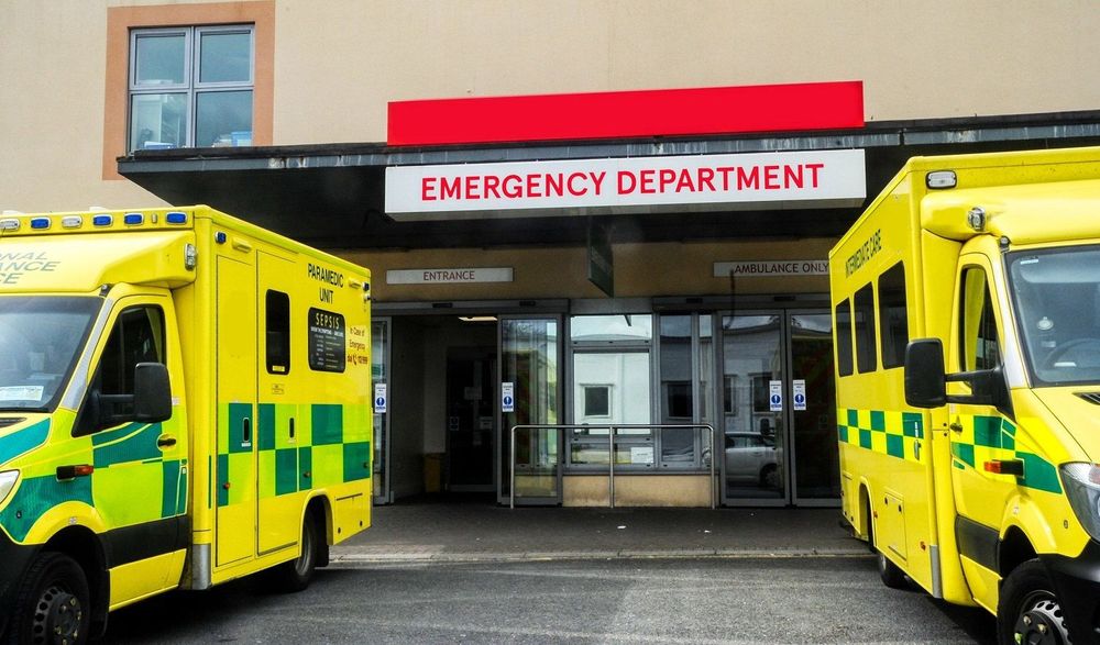 Two ambulances parked outside an NHS hospital emergency department entrance.