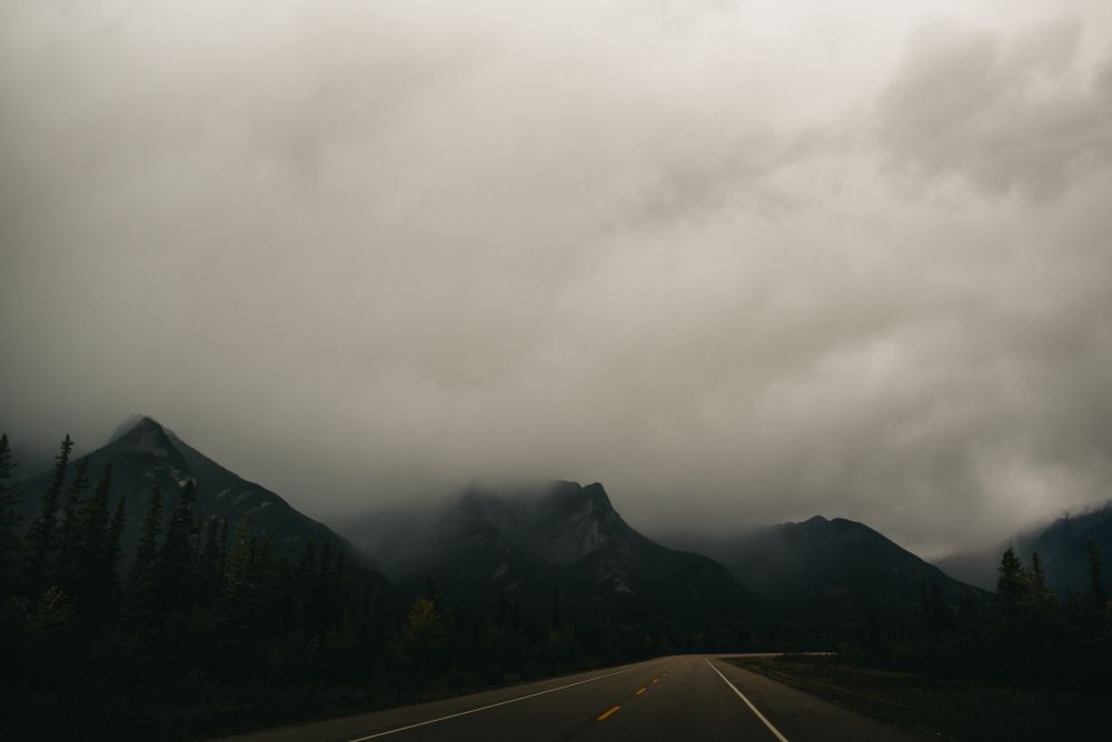 Canadian Rocky Mountains, 3 peaks along a road with low clouds around the peaks