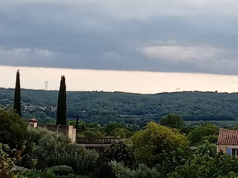 Two Mediterranean conifers to the left; bottom half is landscape; upper half is sky with heavy dark straight-line cloud.