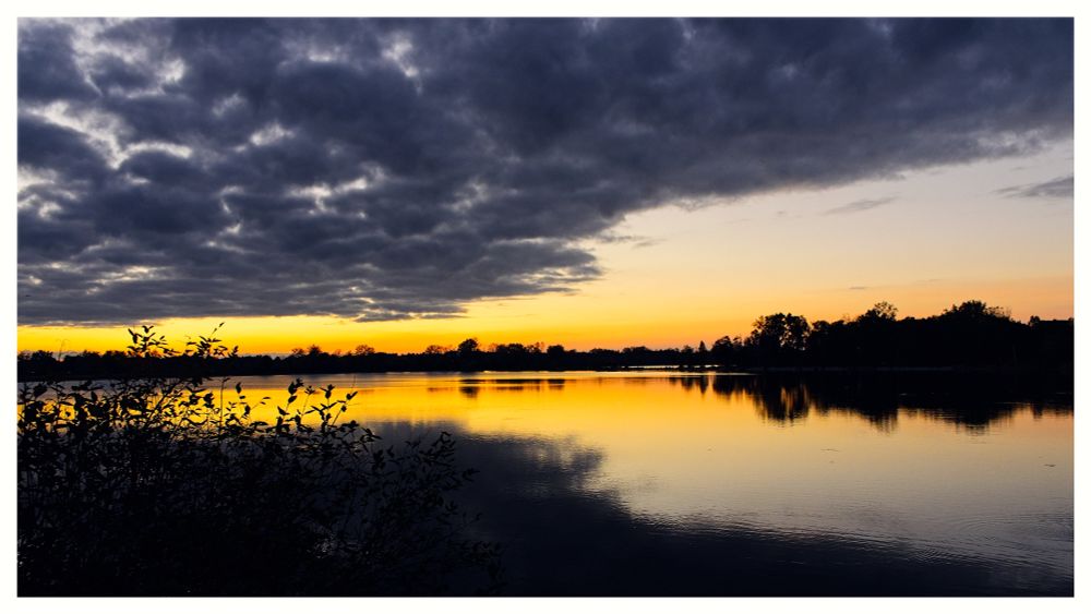 Sunset over the water with a dark cloud cover obscuring the orange setting sun.