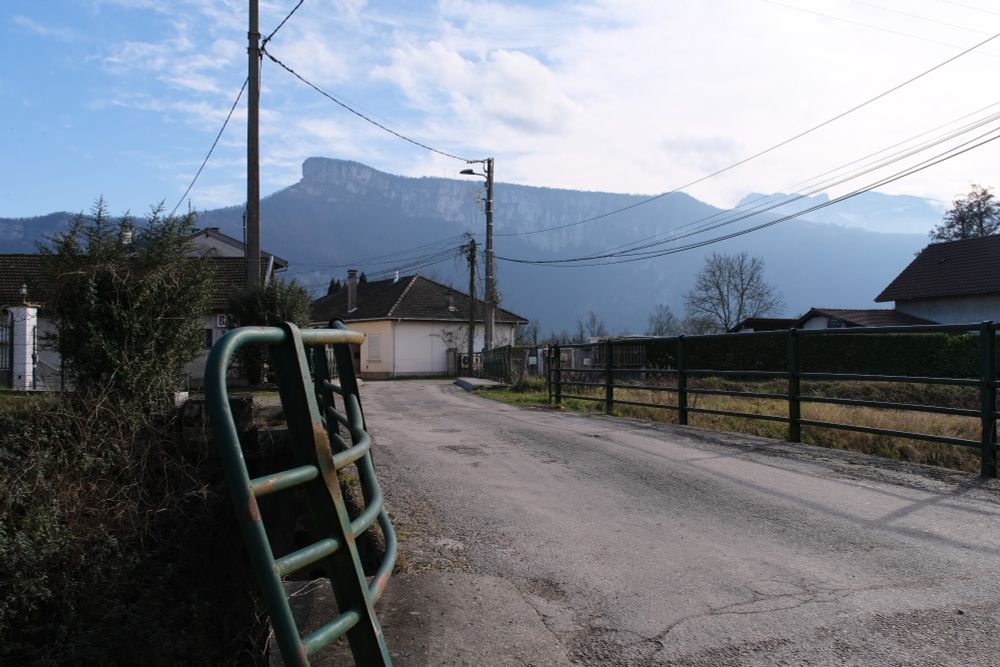 A bridge through a rural town bends slightly around the river curve with a mountain ridge visible against a blue sky