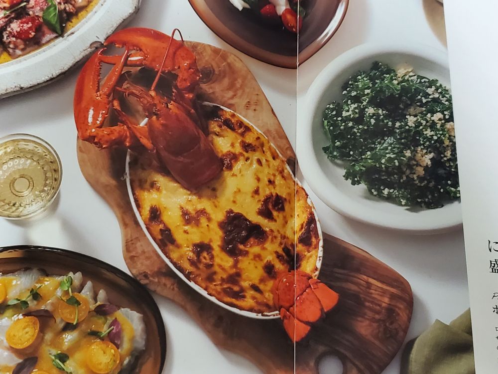 ディーンアンドデルーカのホリデーコレクション2025(冊子)の見開き、ロブスター一尾をまるまる使ったロブスターグラタンが中央に置かれたクリスマスディナーテーブルの写真。