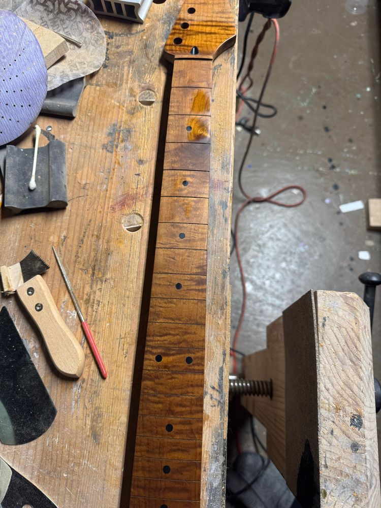 A guitar neck sitting on a bench. 