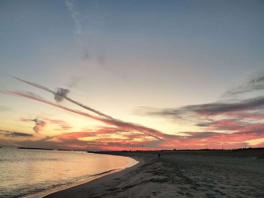 夜明けの砂浜と空。東の空の下方にある雲が朱色に染まっている。
