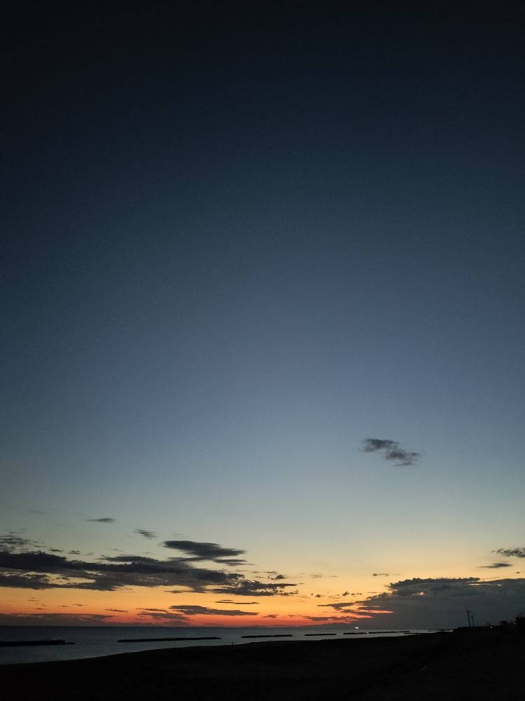 ギリギリ夜明けの空と海。黒からグレー、オレンジのグラデーションの空と、真っ黒な砂浜。