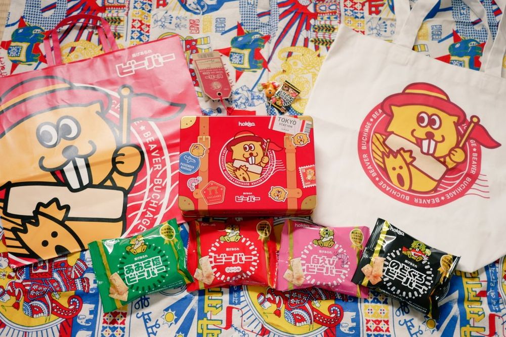 北陸製菓の揚げあられ、「ビーバー」のグッズいろいろ。缶素材のトランク、トートバッグ、トランクの中に入っていたいろんな味のビーバーの小袋が4種類、それらを買ったときに入れてくれた紙袋が並べられている。