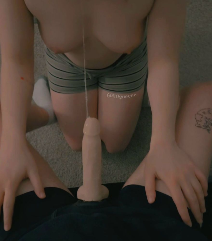 A picture of me on my knees. I'm wearing striped sage green, black, and white boxers and my tits are out. I'm sucking someone's strapon and my thighs are resting on his thighs. His strap is sticking out from his black boxers. A string of spit is connecting his strap to my mouth.