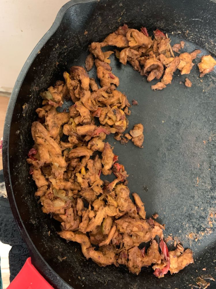 A cast iron pan with golden brown chicken looking things that are actually soy curls, also some small pepper slices cooked with them