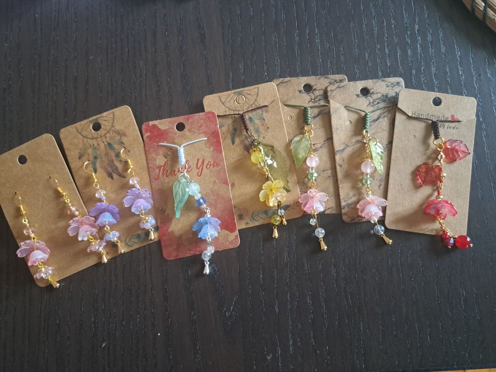 An assortment of earrings and charms with similar lotus-like flowers, in pink, purple, blue, yellow and red