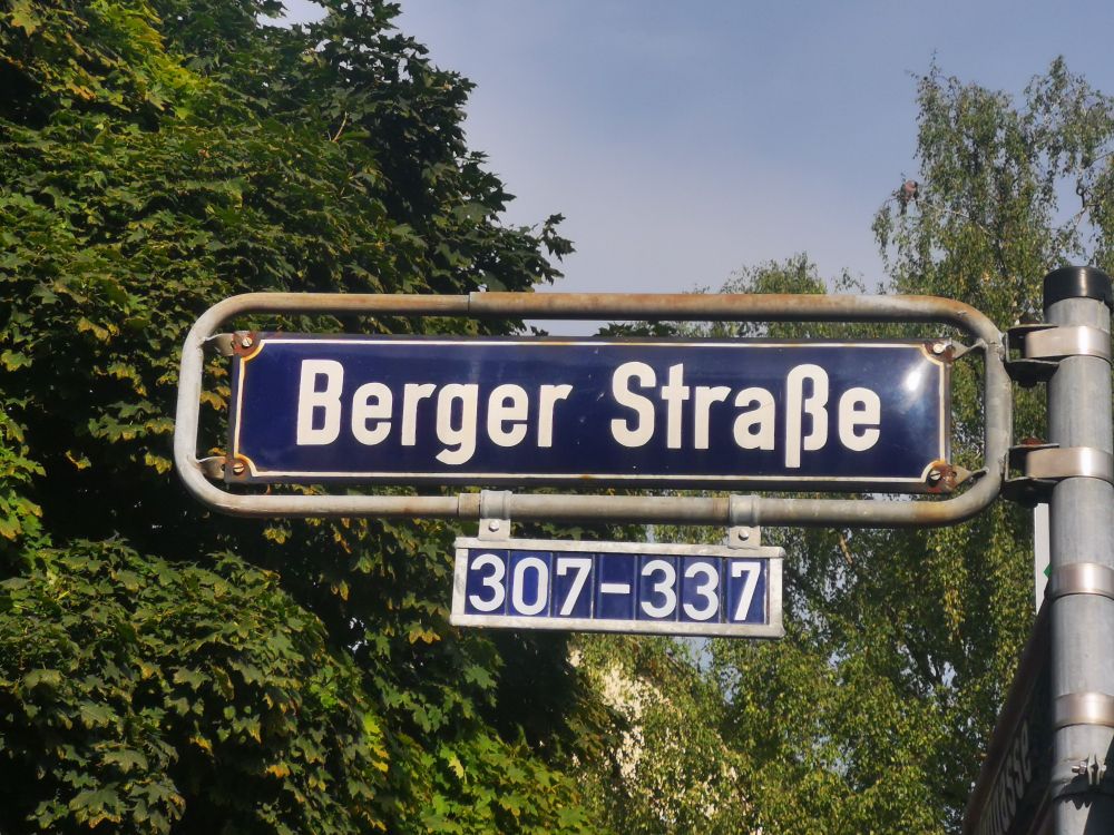 Straßenschild der Berger Straße in Frankfurt am Main, aufgenommen bei Tageslicht mit grünem Laub im Hintergrund.