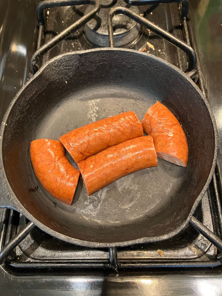 Sliced andouille sausage frying up in a cast iron skillet. The pieces are arranged in the shape of the logo of Wu Tang Clan.