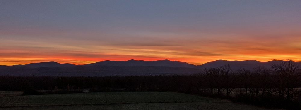 Streaks of yellow, gold, bright rose and dusty purple lie between dark mountains and a grayish blue sky.