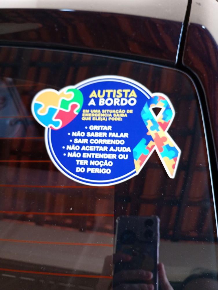 Adesivo colado em um automóvel com instruções sobre possíveis reações atípicas que um autista pode ter em situações de emergência 