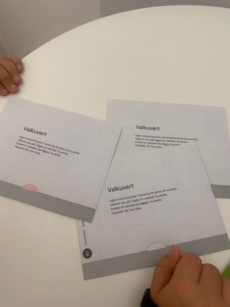 Bild på tre ifyllda valkuvert. Små barnhänder i utkanten av bilden. 