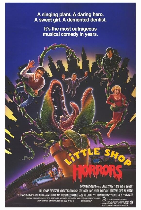 The 1986 movie poster for Little Shop of Horrors features the principal actors being manhandled by the tentacular vines of a giant, carnivorous plant. The man-eating plant, Audrey II, in a giant terracotta planter, is centered with her gaping maw of teeth and tongue against a backdrop featuring the silhouette of a major city skyline backlit in glowing yellow against a background of purples: light at the bottom, dark at the top. Underneath the purple-bordered skyline is a storefront with a teal-and white 50's convertible, perhaps a 1957 Chevrolet Bel Air, parked out front. The musical's Chorus trio lean against the car. The principal actors include Rick Moranis, Ellen Greene, and Steve Martin. The title is printed at the bottom of Audrey II's planter, with "Little Shop" arcing in yellow letters above "of" in blue font, and then "Horrors" in a red font that looks like it's dripping blood. At the top of the poster, in white font, it reads, "A singing plant. A daring hero. A sweet girl. A demented dentist. It's the most outrageous musical comedy in years." At the bottom of the poster, in smaller white font, is the various movie and distribution information. 