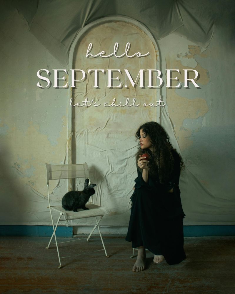 Photograph by Mohamed Weaam of a woman with long, curly hair sitting in a folding chair, in a long black dress, holding a red apple. She's looking down to her right at a black rabbit, sitting in another white folding chair, tilting their head in her direction. Text on the image reads, "hello September. Let's chill out."