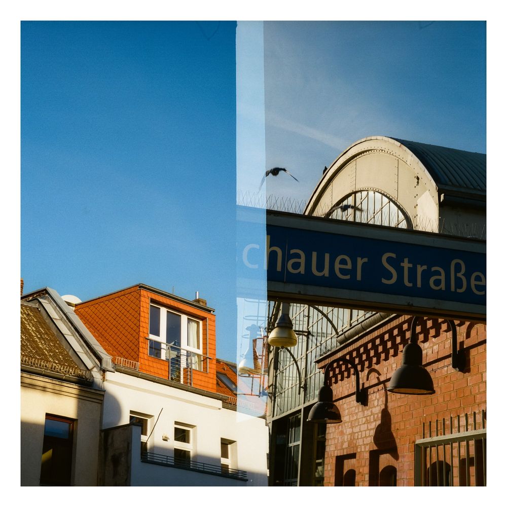 A square color photo split in two: left the roof of a house, right a sign of Berlin train station Warschauer Straße. 