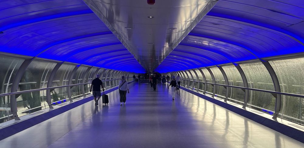 A retrofuturistic skybridge in Manchester, UK, looks like a science fiction set, with jetstream cross section, techno highlights, and driving rain outside.