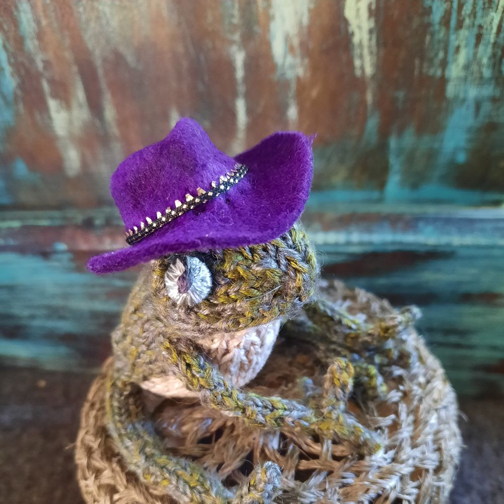 A knitted tog frog wearing a purple Fedora (cowboy hat)