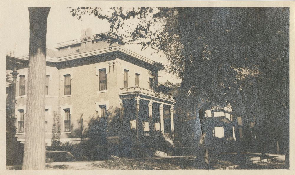 Black and white photograph of brick house at 909 N. Fifth Street in Burlington, Iowa; home of Mr. and Mrs. E. M. Eisfeld, parents of Ada Eisfeld Strause Nelson; porch with balcony above at front entrance; trees at right and left.