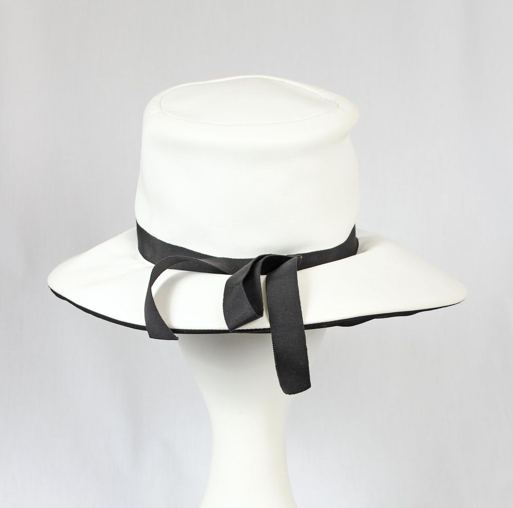 Hat of soft white leather with a black grosgrain hatband and bow: high, flat crown; large flexible brim; fully lined.