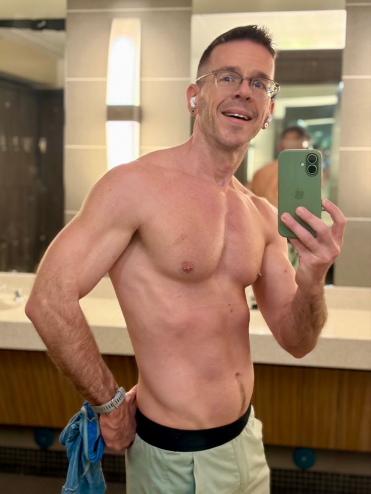 Mirror selfie in a locker room, shirt off, one hand on my hip