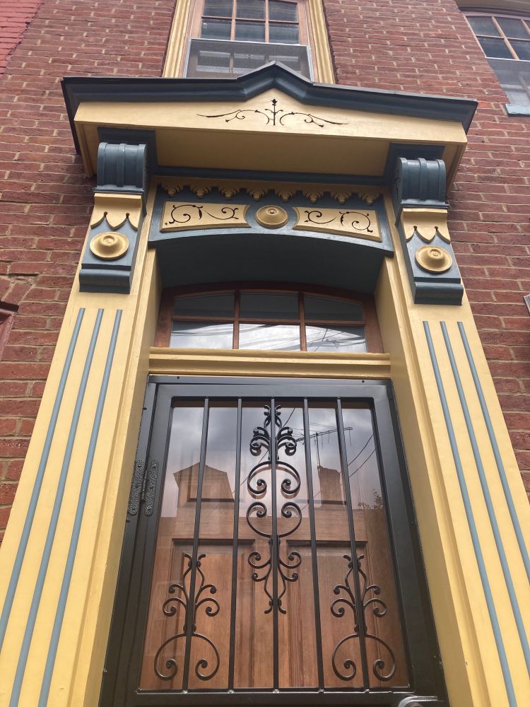 An outer closed door of a house, seen from the outside, with a yellow frame and detailed arch above the door