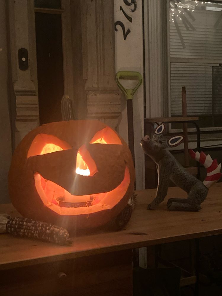 A Jack o lantern sitting on a table, with a painted wolf figurine sitting to the right of it 