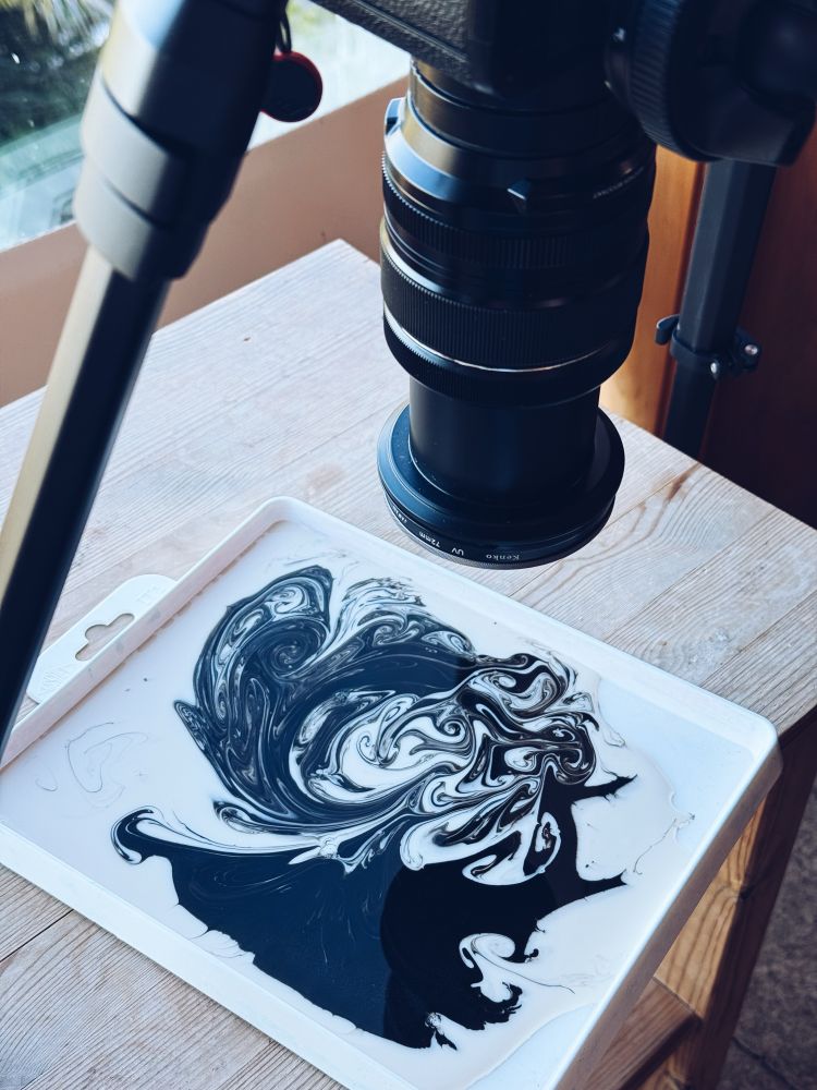 Behind the scene of black ink swirls in a pool of milk captured by a camera. 