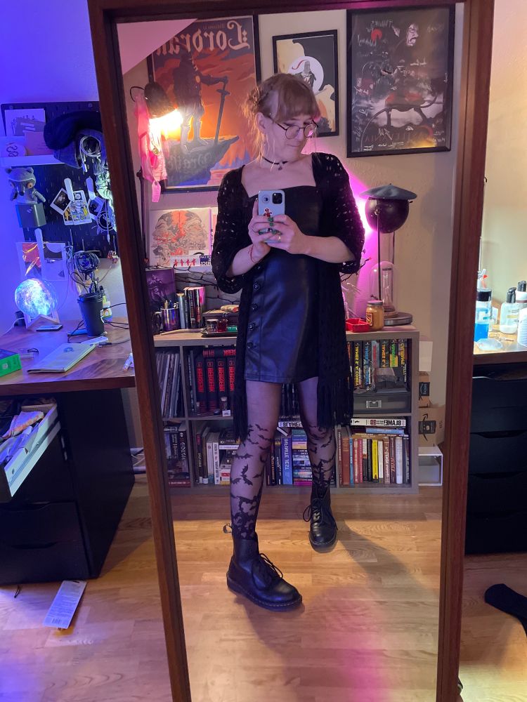 an adult trans girl wearing a leather dress, doc martens, and bat tights