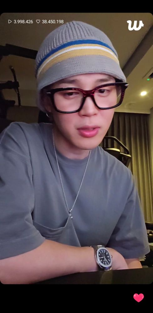 Jimin of BTS in grey t-shirt and grey hat, dark rimmed square glasses doing his birthday live on Weverse