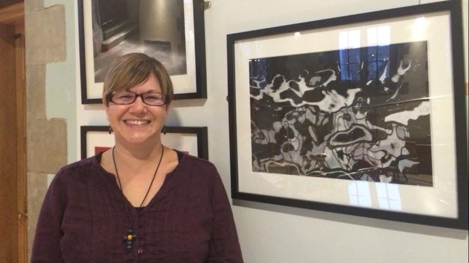 Me standing next to a close up photo of water taken from a bridge. The mixture of the reflection of the bridge in the ripples of the water and the foam make an interesting pattern. The photo is black and white. 