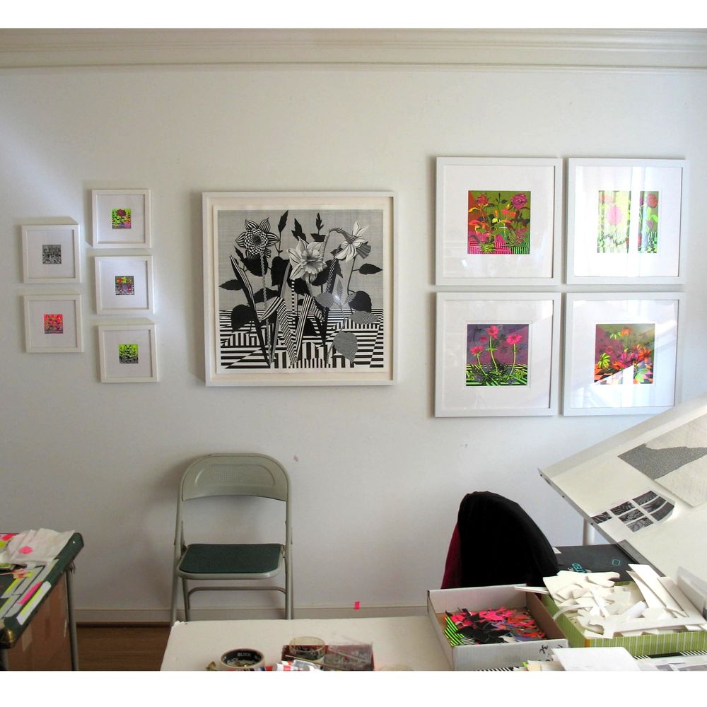 White wall in an artist studio with a variety of intensely patterned, framed artworks. All works portray flowers, and the largest piece in the middle is black and white with daffodils.